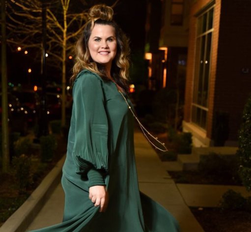 A photo of our resale shop manager, Katie Rockwell, wearing a long green dress, smiling at the camera.